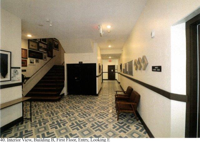 After: Interior view of school entrance foyer facing east with stairs to left and corridor retained straight ahead. Existing red quarry tile floors are replaced with a white and blue patterned tile.